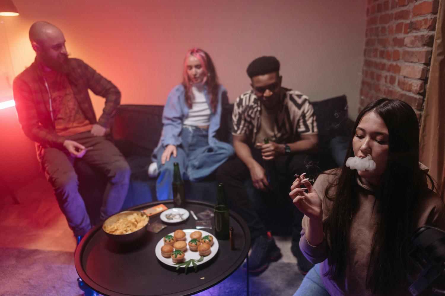 Adults gathered in a lounge while one person smokes cannabis in a relaxed 420-friendly environment.