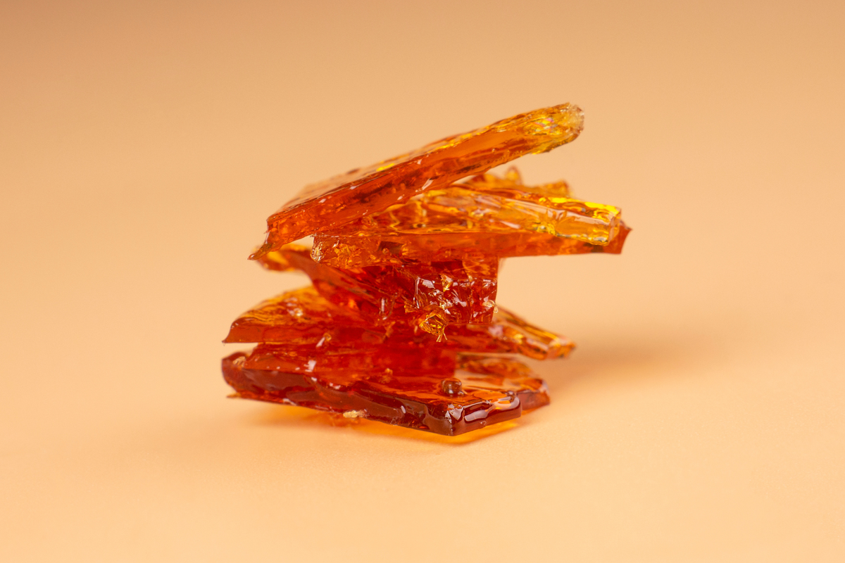 Thin pieces of amber weed shatter stacked against a warm background.