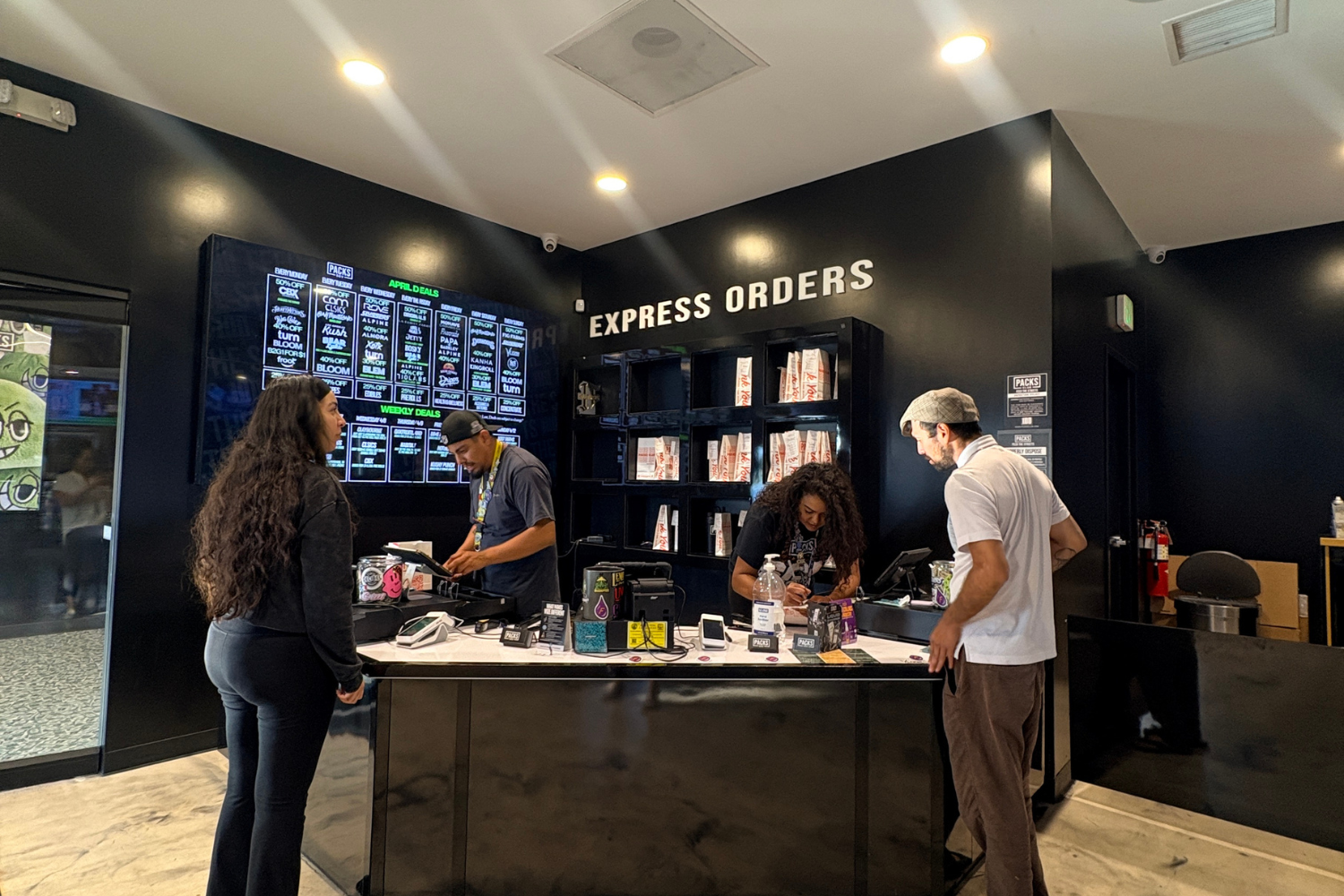 Customers ordering cannabis products at a sleek black dispensary counter in Los Angeles with digital menus and express order signage.