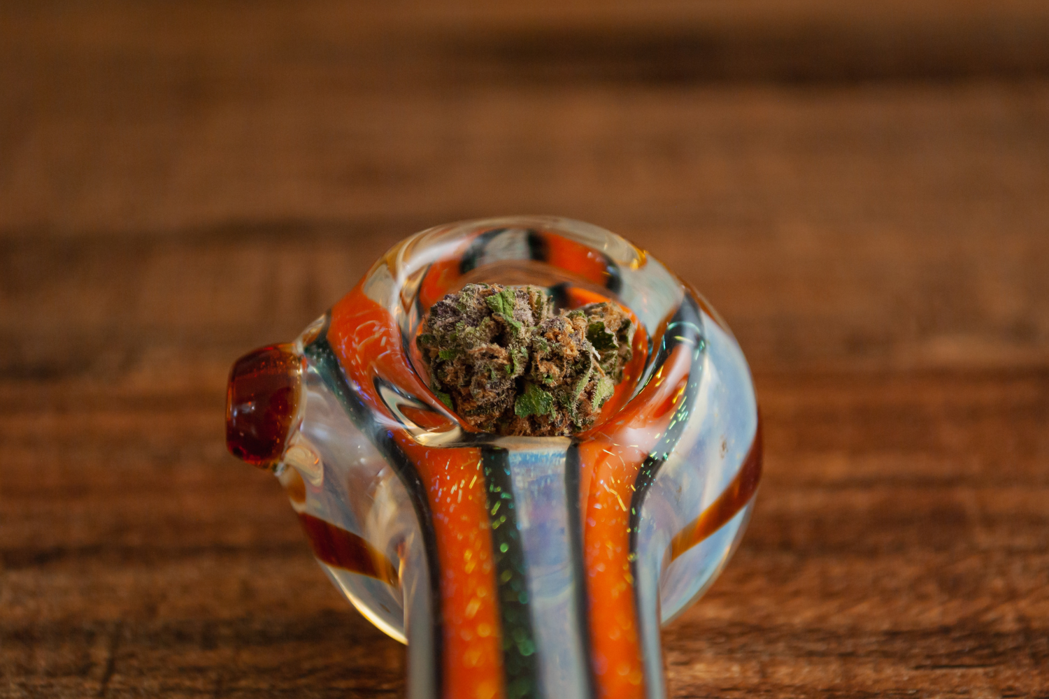 Close-up of a colorful glass smoking pipe on a wooden surface, focusing on the bowl part of the pipe.