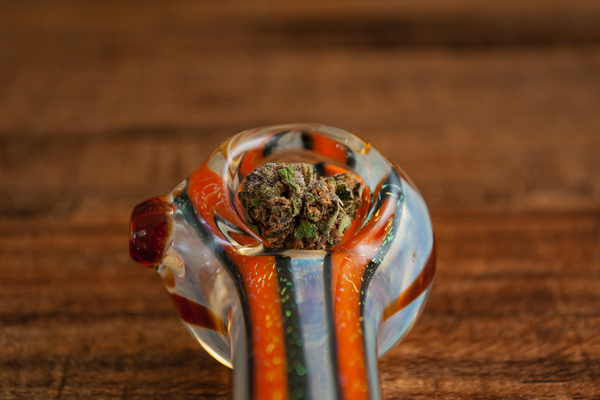 Close-up of a colorful glass smoking pipe on a wooden surface, focusing on the bowl part of the pipe.