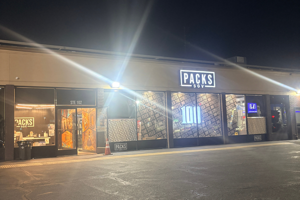 Exterior view of a modern legal cannabis dispensary storefront named Packs SGV illuminated by bright overhead lights at night.
