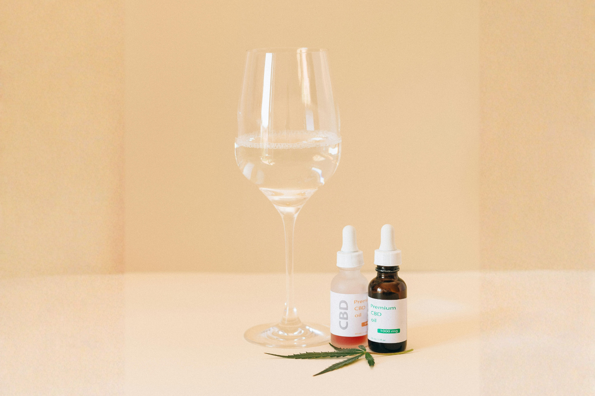 Cannabis tincture bottles beside a wine glass and cannabis leaf on a neutral background.