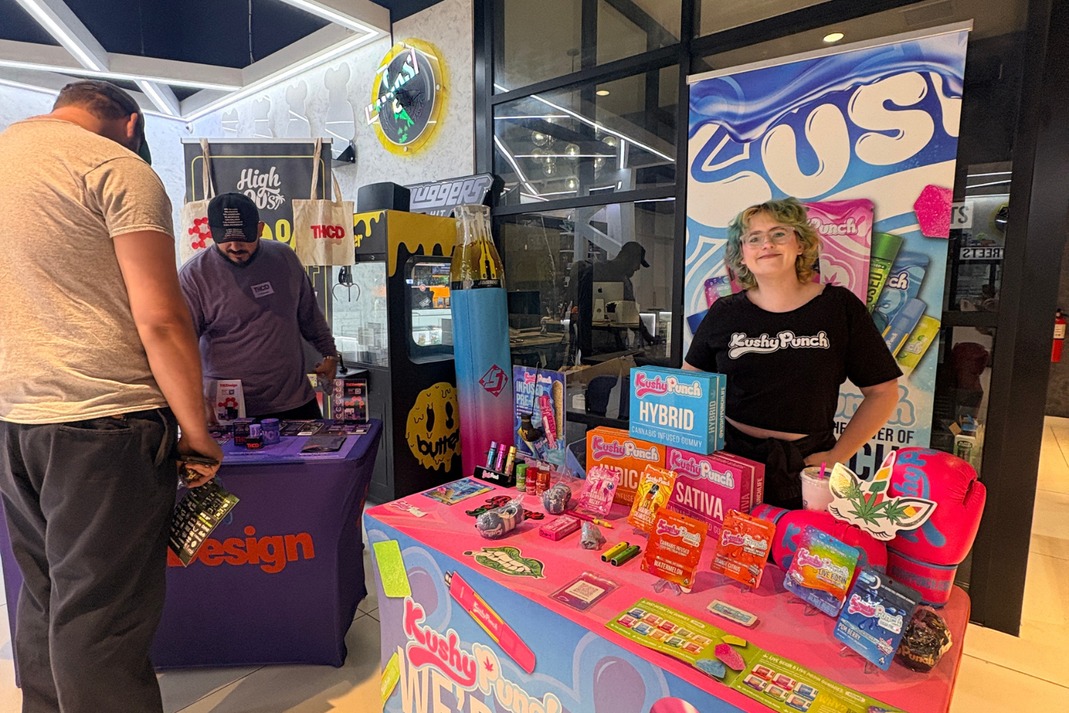 Cannabis brand representatives operating colorful vendor booths at an indoor cannabis festival.