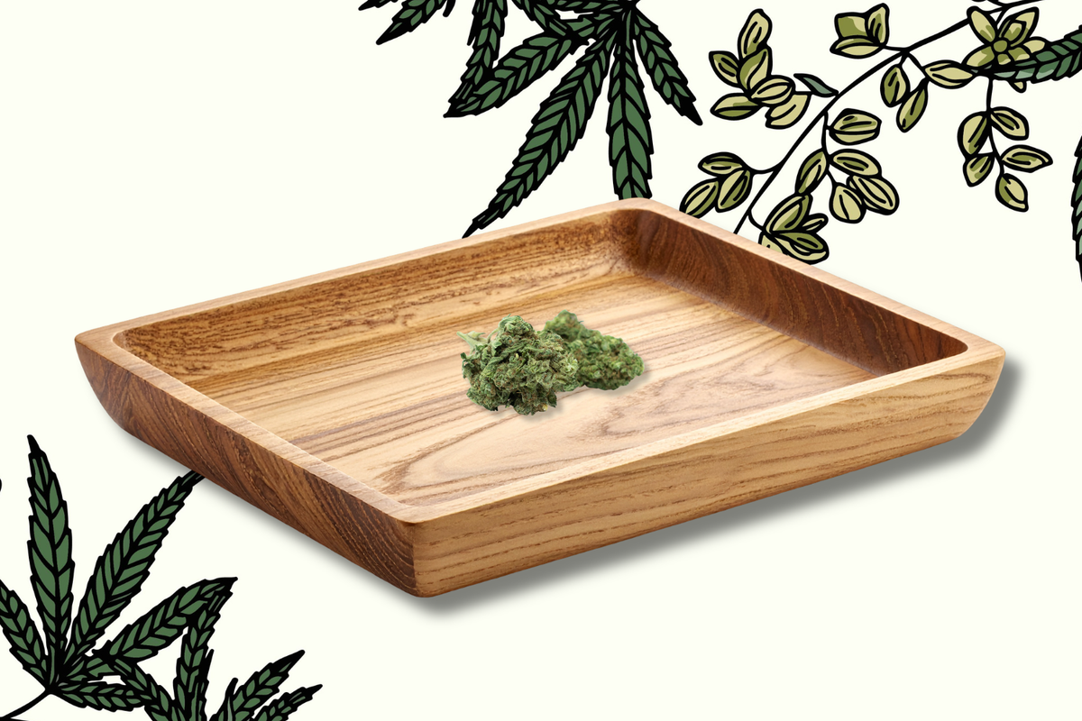 Wooden weed tray with raised edges holding cannabis buds against a background of illustrated leaves.
