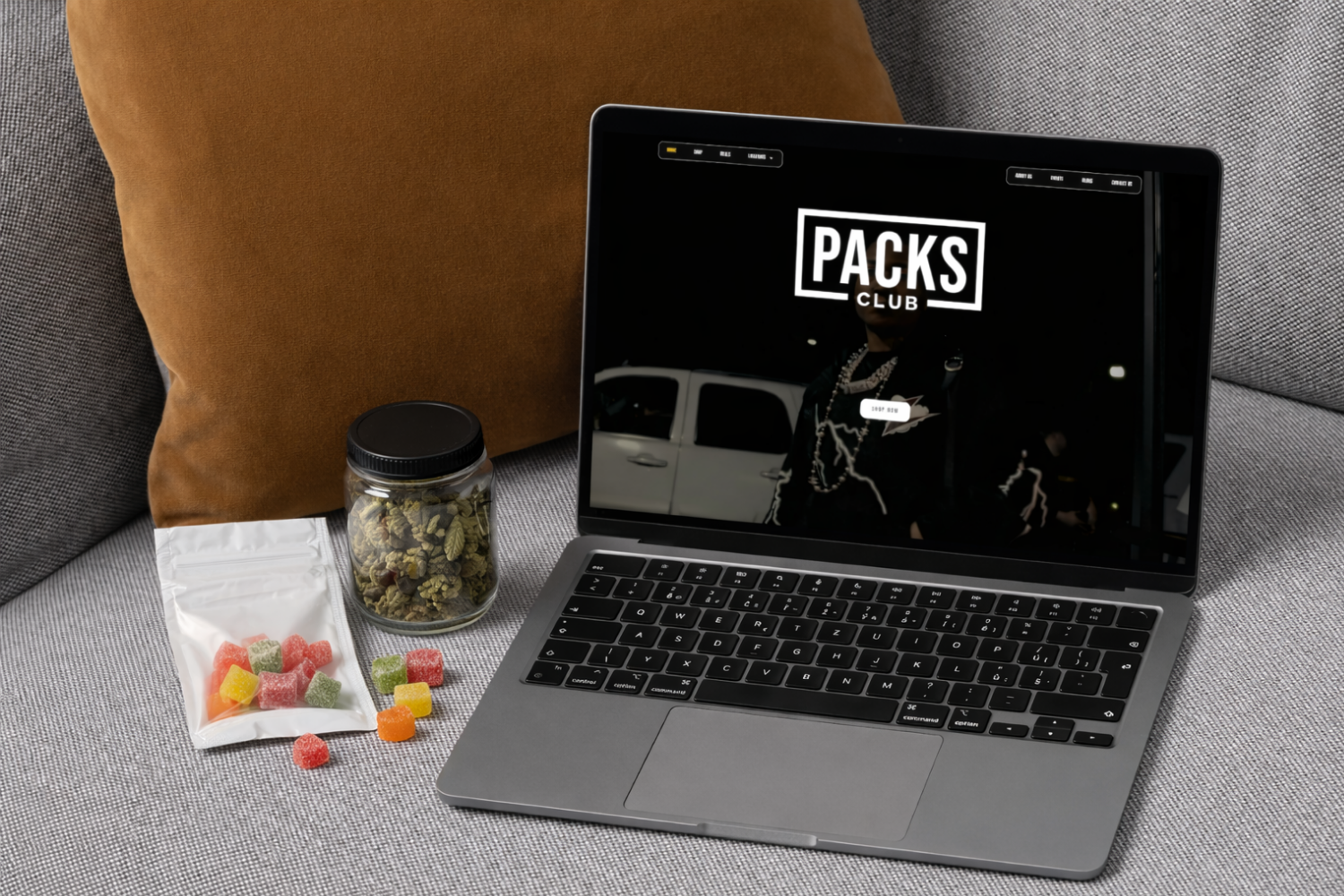 Laptop showing Packs Club homepage beside a jar of cannabis flower and THC gummies on a sofa