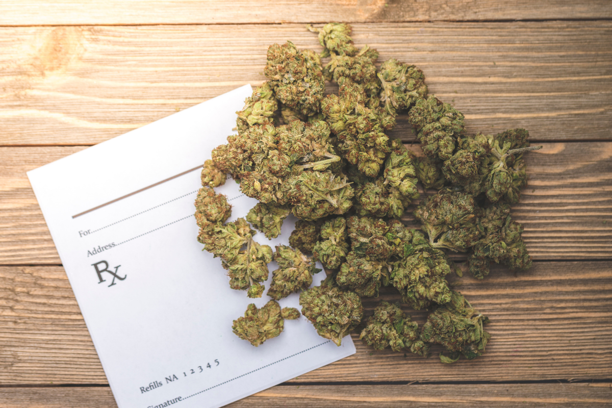 Cannabis buds spread across a medical prescription form on a wooden surface.
