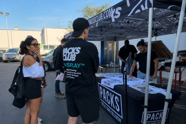 Guests speaking with PACKS Club representatives beneath a branded event tent.