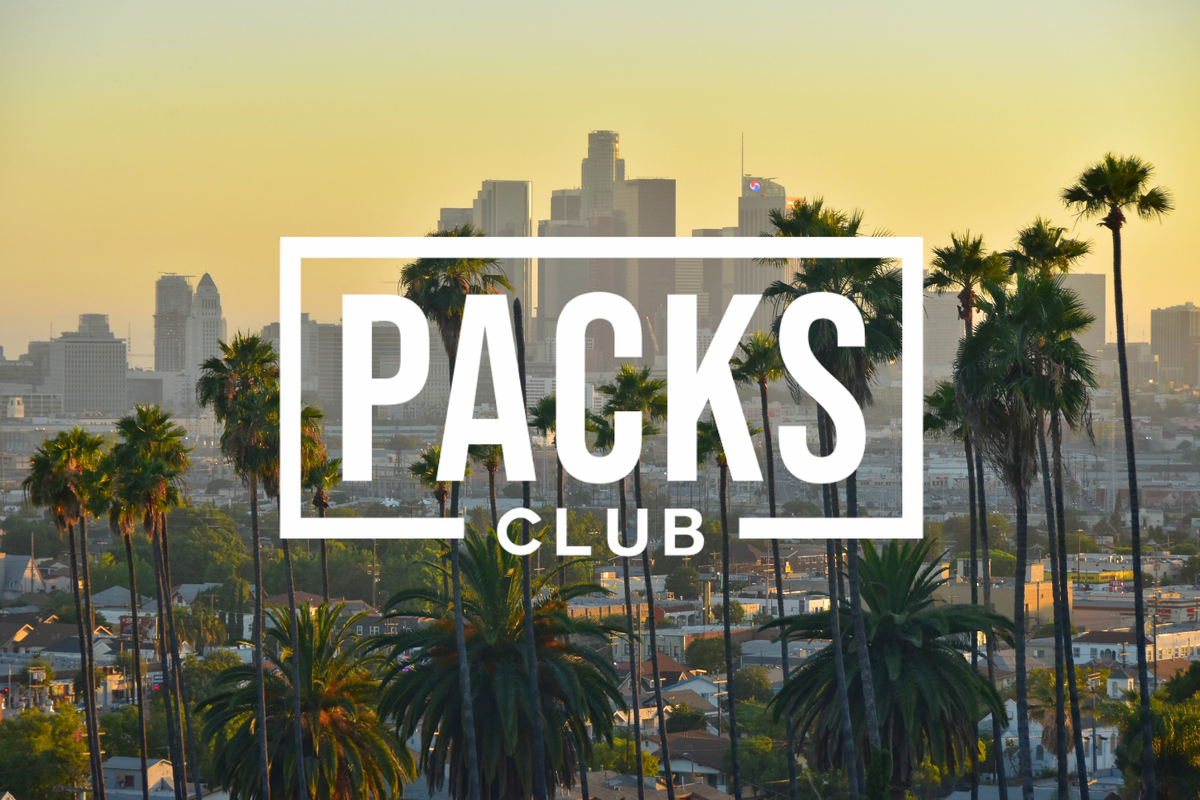 Sunset view of downtown Los Angeles with palm trees in the foreground and skyscrapers in the distance. Overlaid white frame contains bold text “PACKS CLUB,” suggesting branding or promotional content.