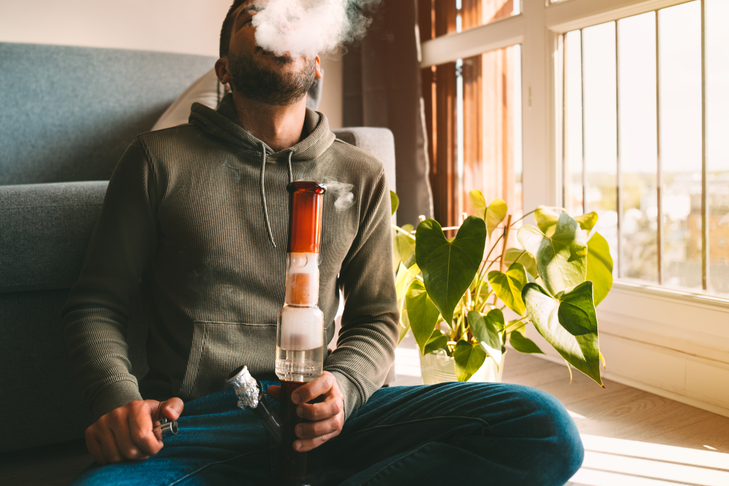 Man smoking bong and exhaling the smoke at home. Man smoking pot, medical marijuana or cannabis from a bong or water pipe.