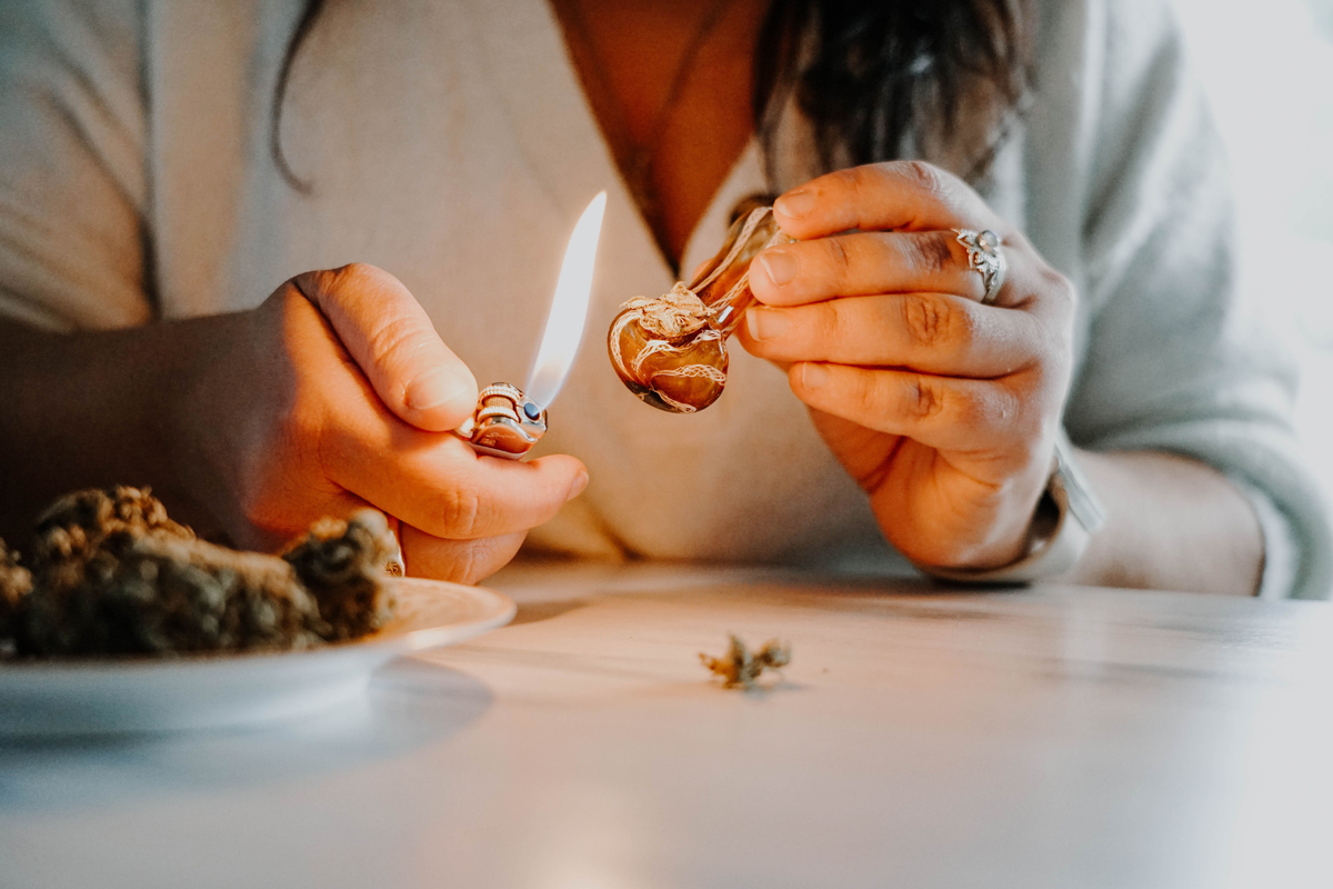 Person using a lighter to ignite cannabis in a glass hand pipe.